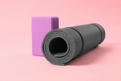 Grey exercise mat and yoga block on pink background