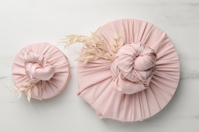 Photo of Furoshiki technique. Gifts packed in pink fabric and dried branches on white marble table, flat lay
