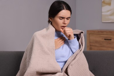 Woman coughing on sofa at home. Cold symptoms