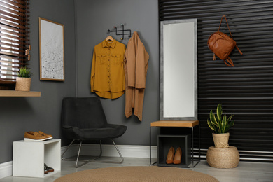 Photo of Hallway interior with modern furniture, mirror and hanging clothes