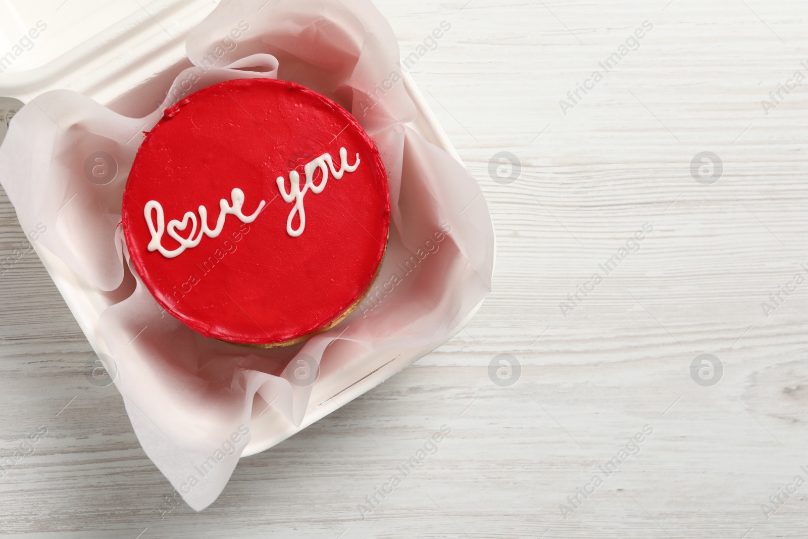 Photo of Bento cake with Love You text in takeaway box on white wooden table, top view. Space for text. St. Valentine's day surprise