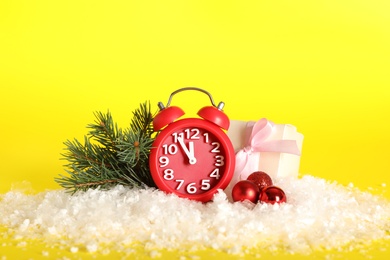 Photo of Alarm clock with Christmas decor on yellow background. New Year countdown