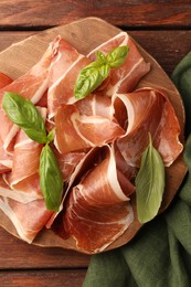 Photo of Slices of tasty cured ham and basil on wooden table, top view