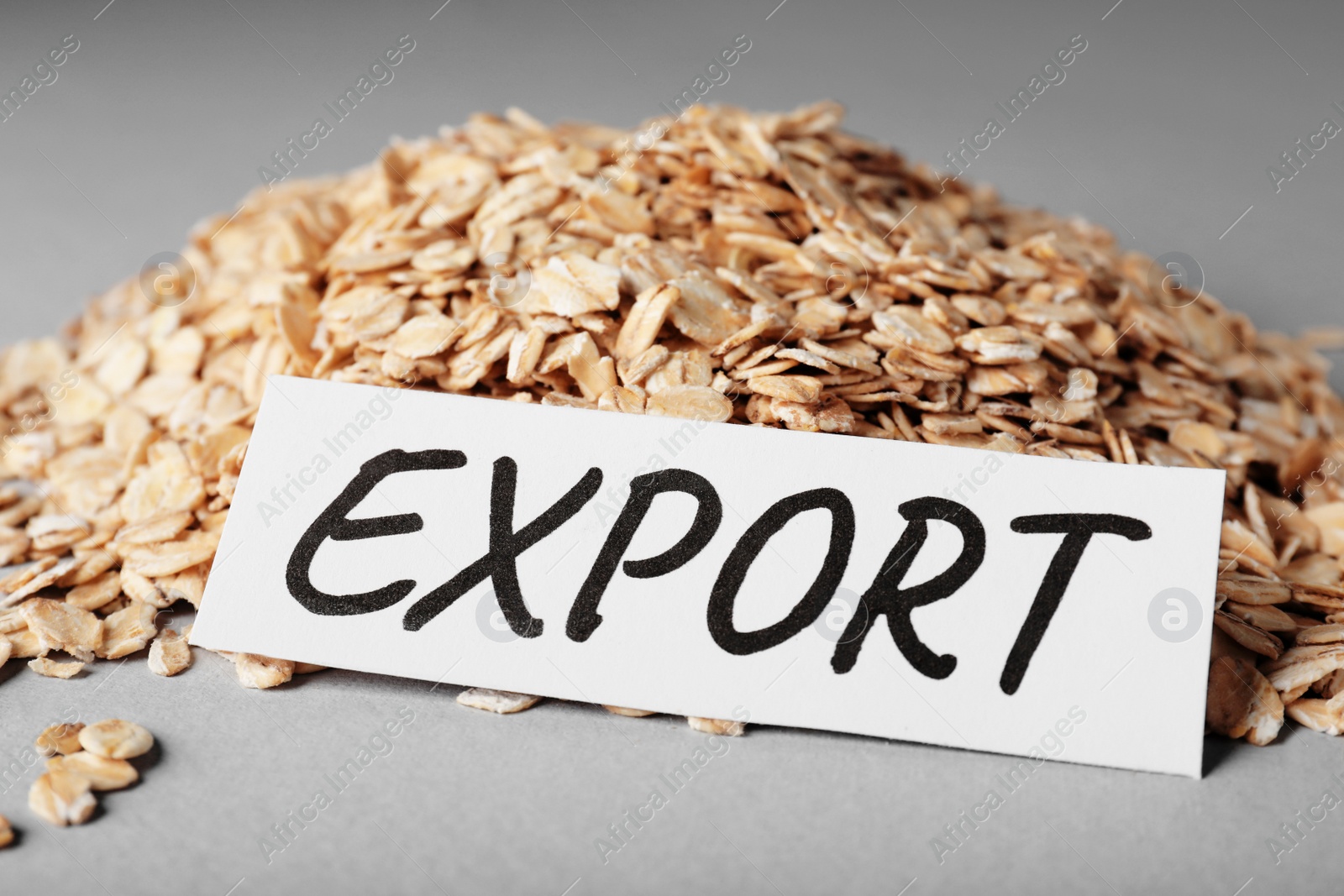 Photo of Pile of oatmeal and paper card with word Export on grey background, closeup