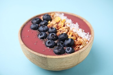 Photo of Bowl of delicious fruit smoothie with fresh blueberries, granola and coconut flakes on light blue background, closeup