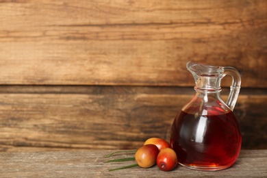 Photo of Palm oil in glass jug and fresh fruits on wooden table. Space for text