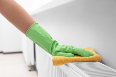 Photo of Woman cleaning radiator with rag indoors, closeup