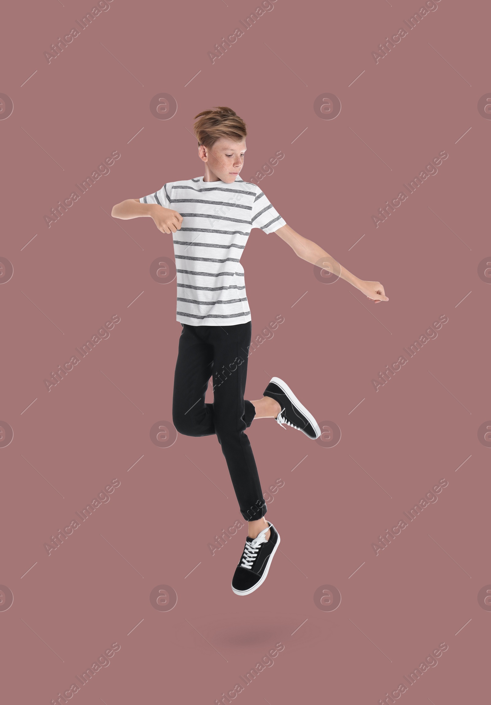 Image of Teenage boy jumping on dusty pink background, full length portrait