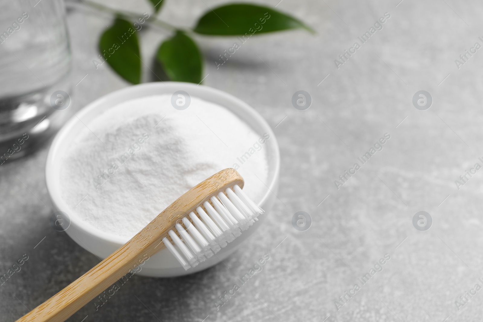 Photo of Bamboo toothbrush, green leaf and bowl of baking soda on grey table, closeup. Space for text