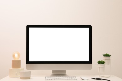 Photo of Comfortable workplace with blank computer display on desk near light wall. Space for text