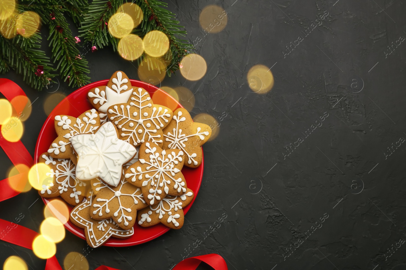 Photo of Tasty Christmas cookies with icing, fir tree branches and ribbon on black table, flat lay. Space for text