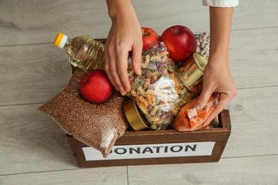 Photo of Woman taking food from donation box on wooden floor, closeup