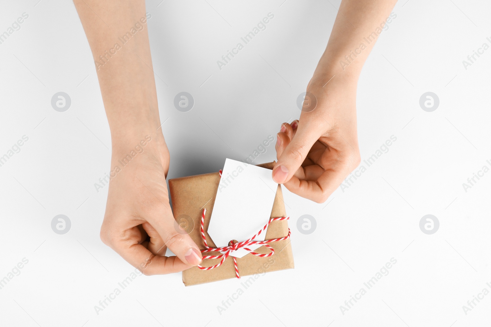 Photo of Woman holding parcel wrapped in kraft paper with tag on white background, top view