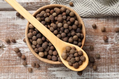 Photo of Aromatic allspice pepper grains in bowl and spoon on wooden table, top view