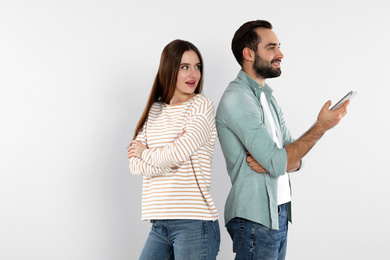 Photo of Man with smartphone ignoring his girlfriend on light background. Relationship problems