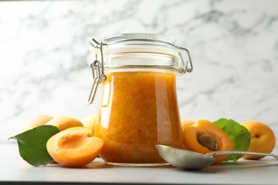 Photo of Jar of apricot jam and fresh fruits on light table