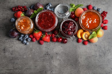 Photo of Jars with different jams and fresh fruits on grey table, flat lay. Space for text