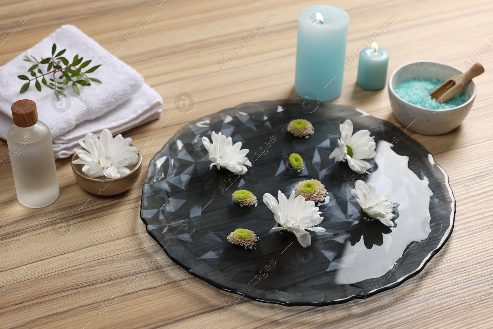 Photo of Plate with water, flowers, burning candles and sea salt on wooden floor. Pedicure procedure