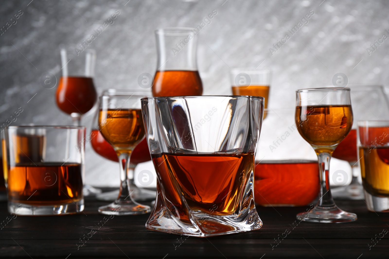 Photo of Different delicious liqueurs in glasses on dark wooden table