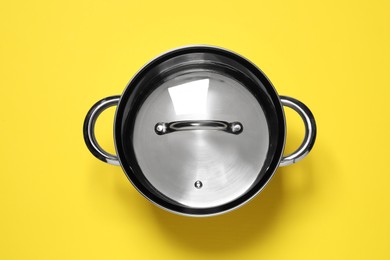 Steel pot with glass lid on yellow background, top view