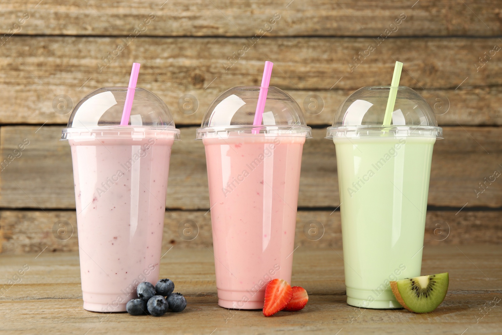 Photo of Plastic cups with different tasty smoothies and fresh fruits on wooden table