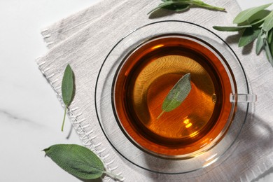 Cup of aromatic herbal tea with sage on white table, flat lay