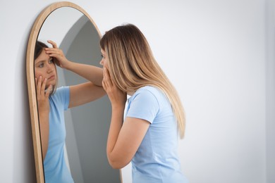 Sleep deprived young woman looking at herself in mirror indoors
