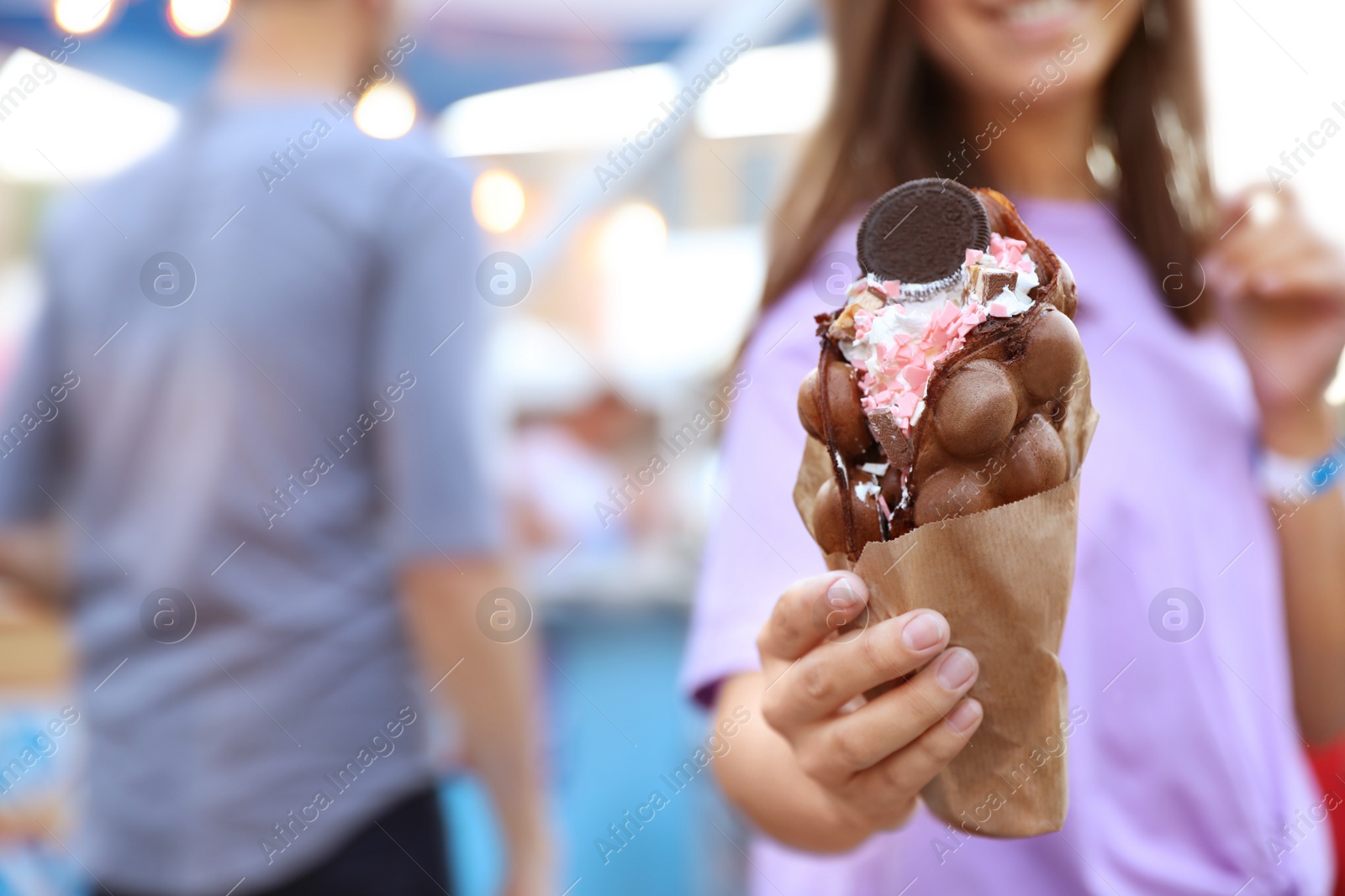 Photo of Young woman holding delicious sweet bubble waffle with ice cream outdoors, closeup