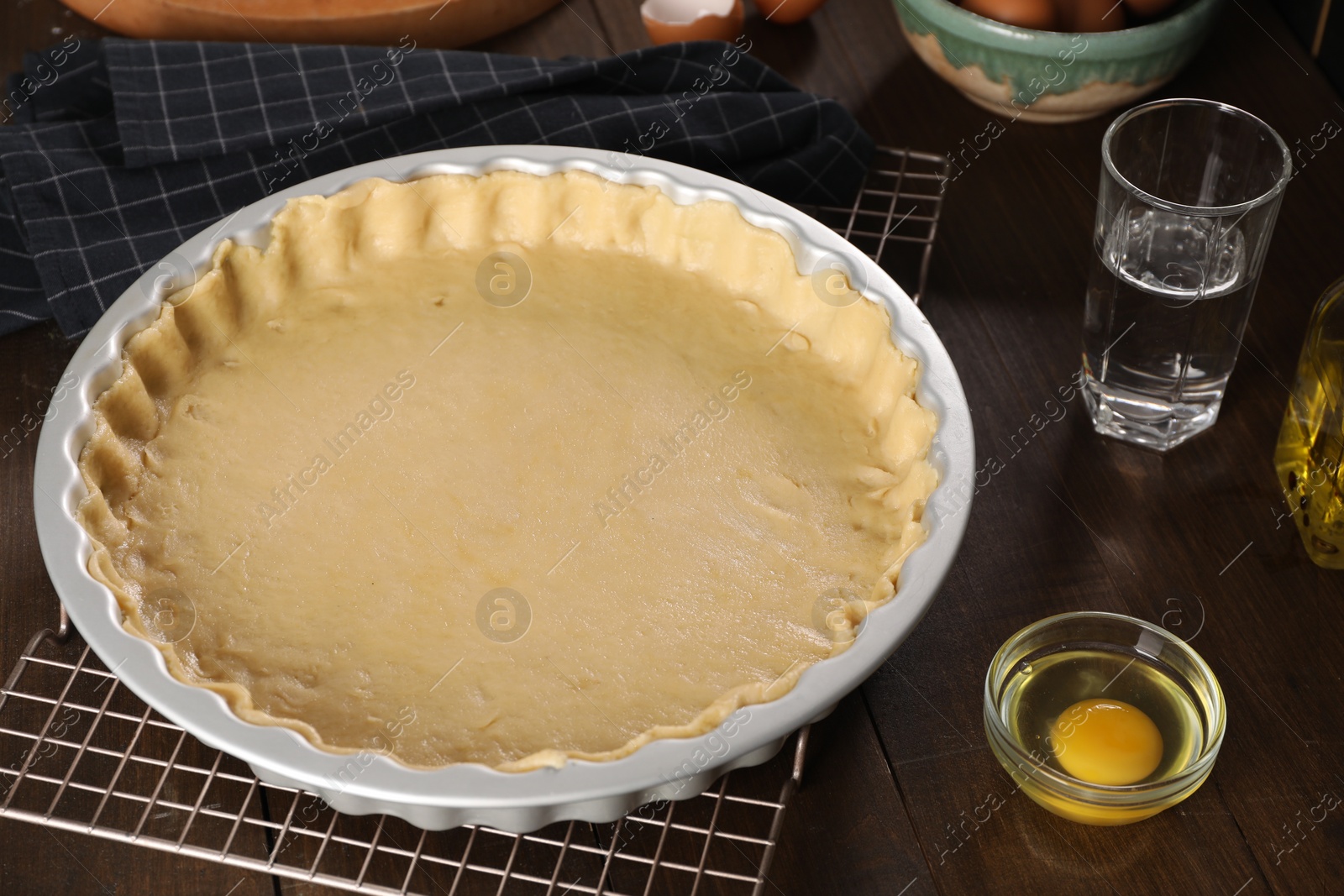 Photo of Pie tin with fresh dough and ingredients on wooden table. Making quiche