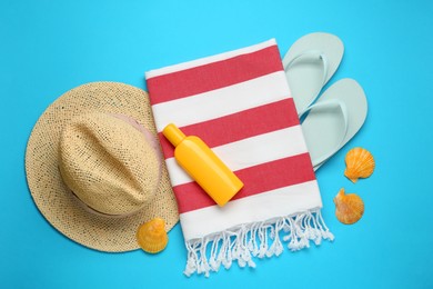 Photo of Beach towel, flip flops, hat and sun protection product on light blue background, flat lay