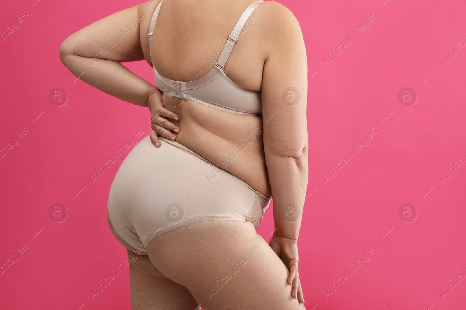 Photo of Overweight woman in beige underwear on pink background, closeup. Plus-size model