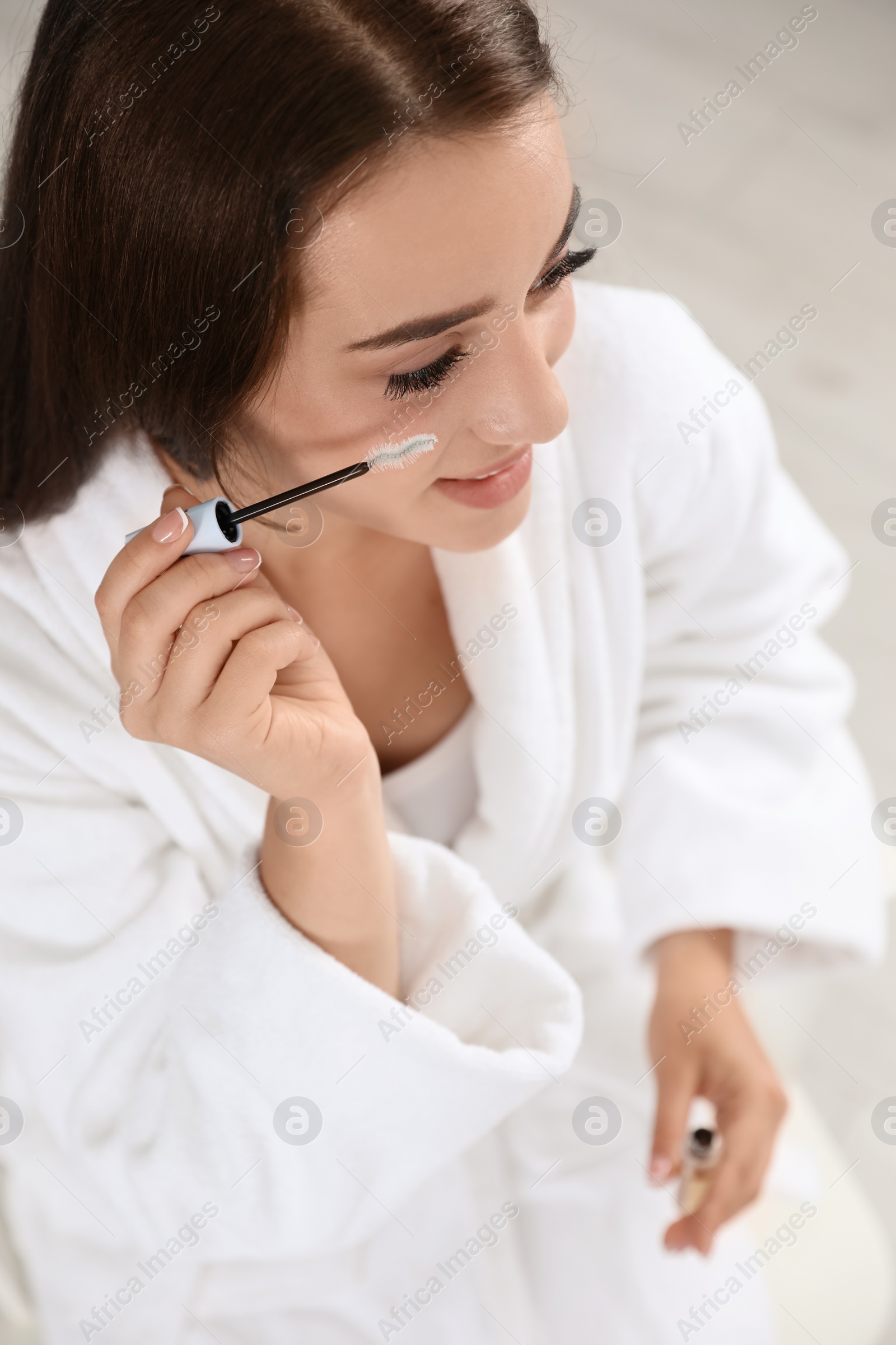 Photo of Attractive young woman applying oil onto her eyelashes indoors