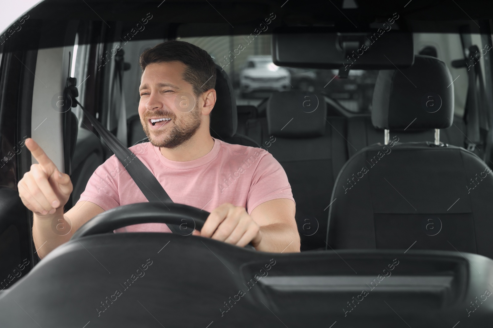 Photo of Listening to radio. Handsome man enjoying music in car, view through windshield