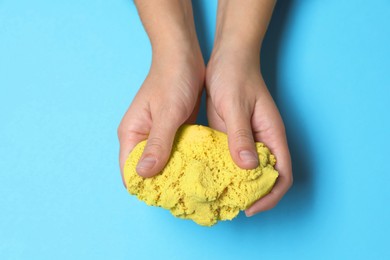 Woman playing with yellow kinetic sand on light blue background, top view