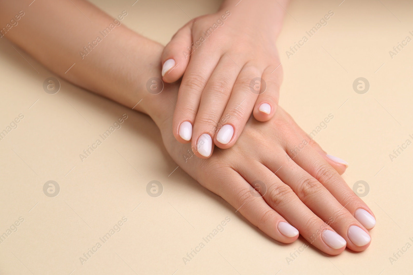 Photo of Woman showing her manicured hands with white nail polish on beige background, closeup