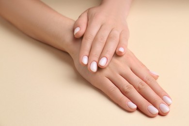 Woman showing her manicured hands with white nail polish on beige background, closeup