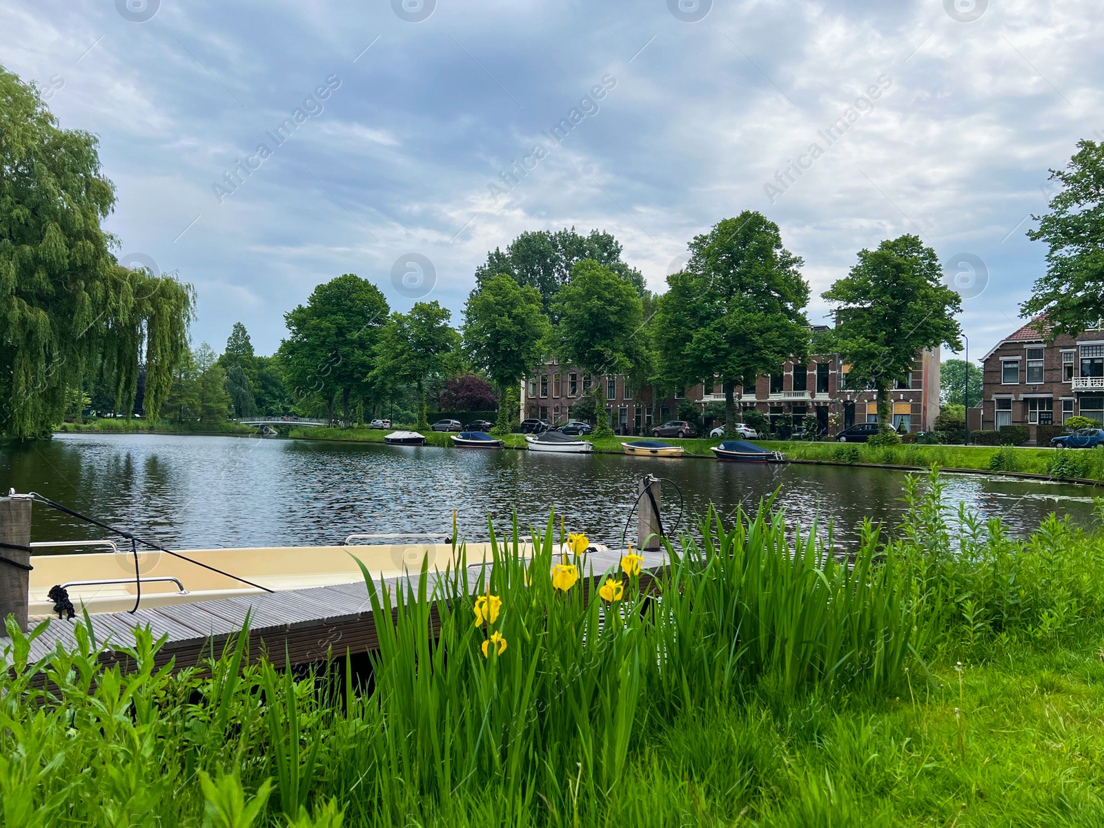 Photo of Beautiful view of city canal with pier and moored boat surrounded by greenery