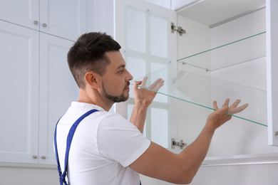 Photo of Worker installing cabinet with shelves in kitchen