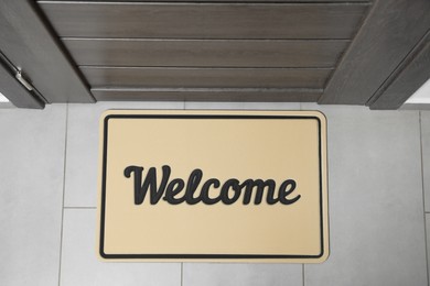 Photo of Beautiful beige doormat with word Welcome on floor near entrance, top view