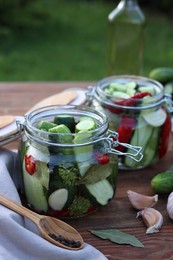 Photo of Glass jars with fresh cucumbers and other ingredients on wooden table. Canning vegetables