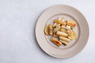 Photo of Plate with baked salsify roots, lemon and thyme on light grey table, top view. Space for text