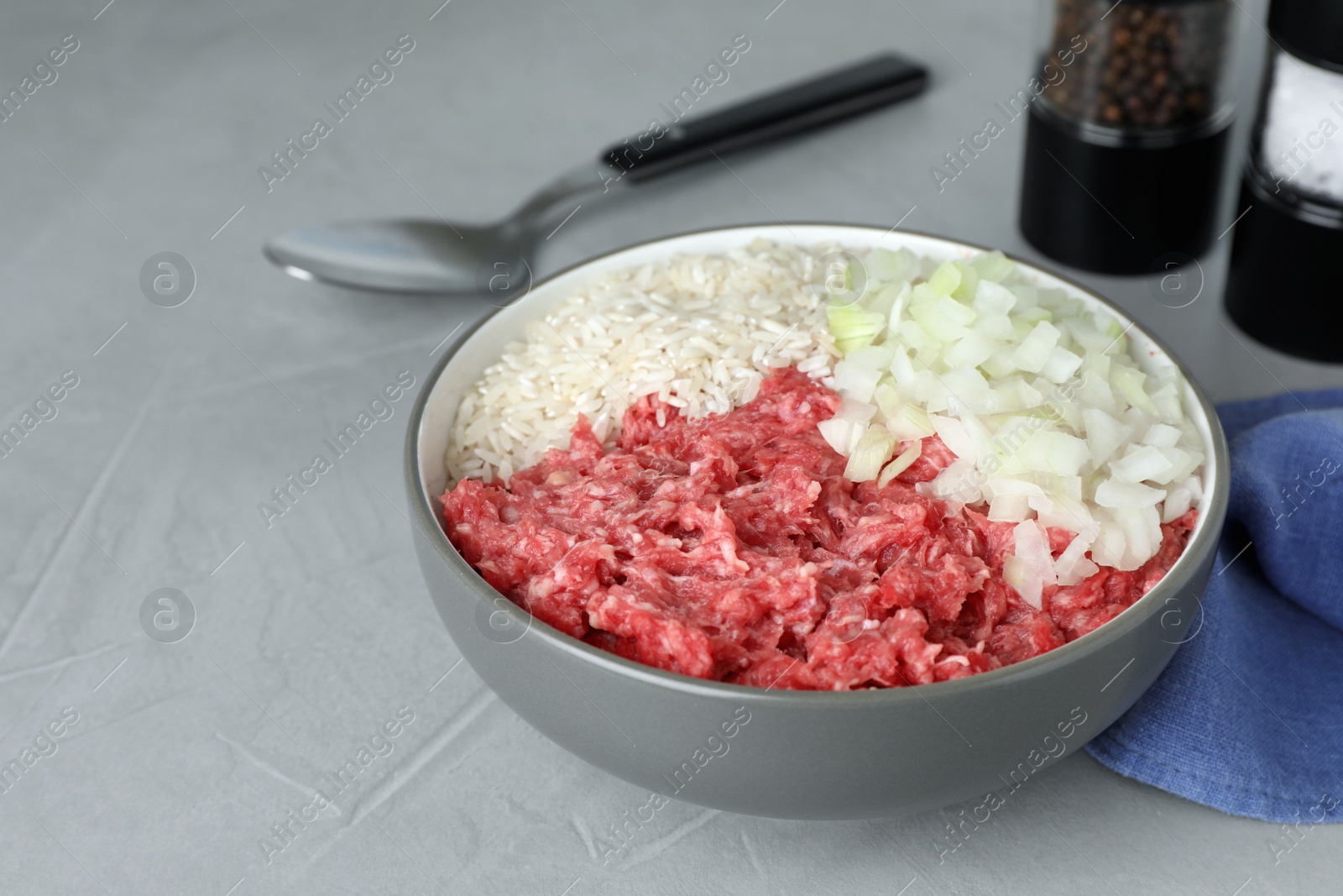 Photo of Bowl of forcemeat, chopped onion with rice for preparing stuffed cabbage rolls on light grey table