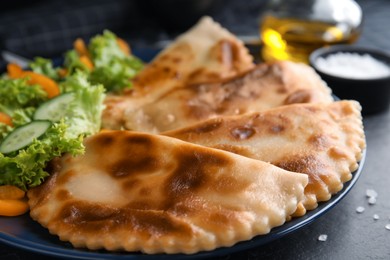 Delicious fried chebureki with vegetables on black table, closeup