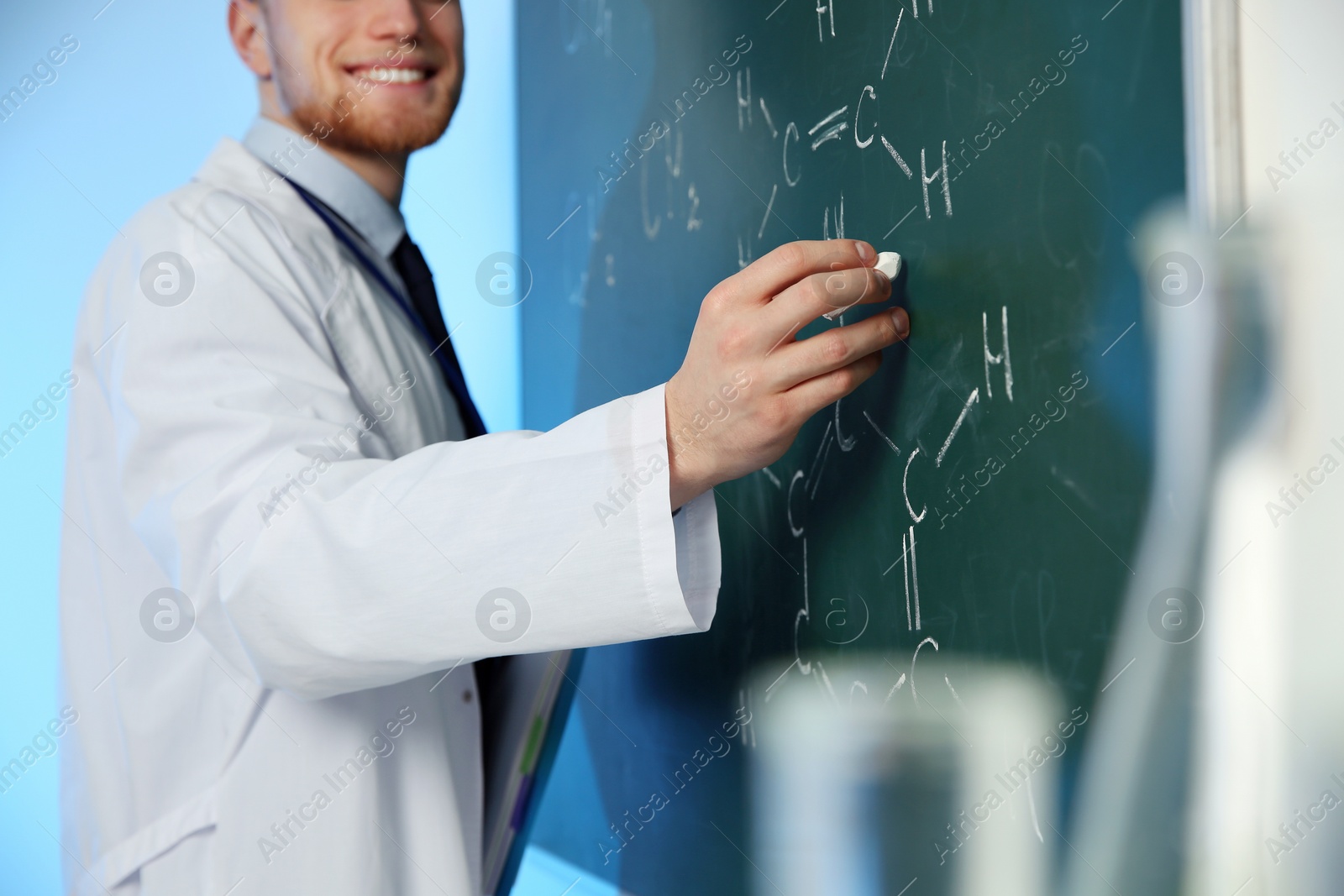 Photo of Male scientist writing chemical formula on chalkboard indoors, closeup