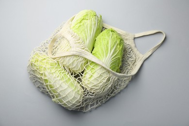 Photo of Fresh Chinese cabbages in string bag on light background, top view