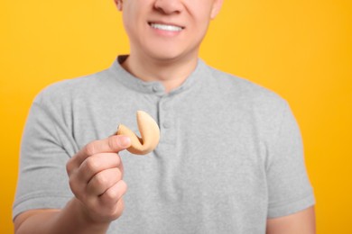 Photo of Happy man holding tasty fortune cookie with prediction on orange background, closeup
