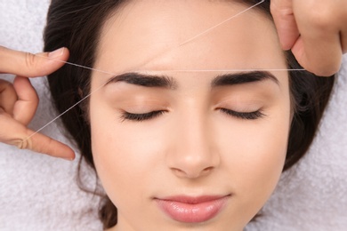 Photo of Young woman having professional eyebrow correction procedure in beauty salon, closeup