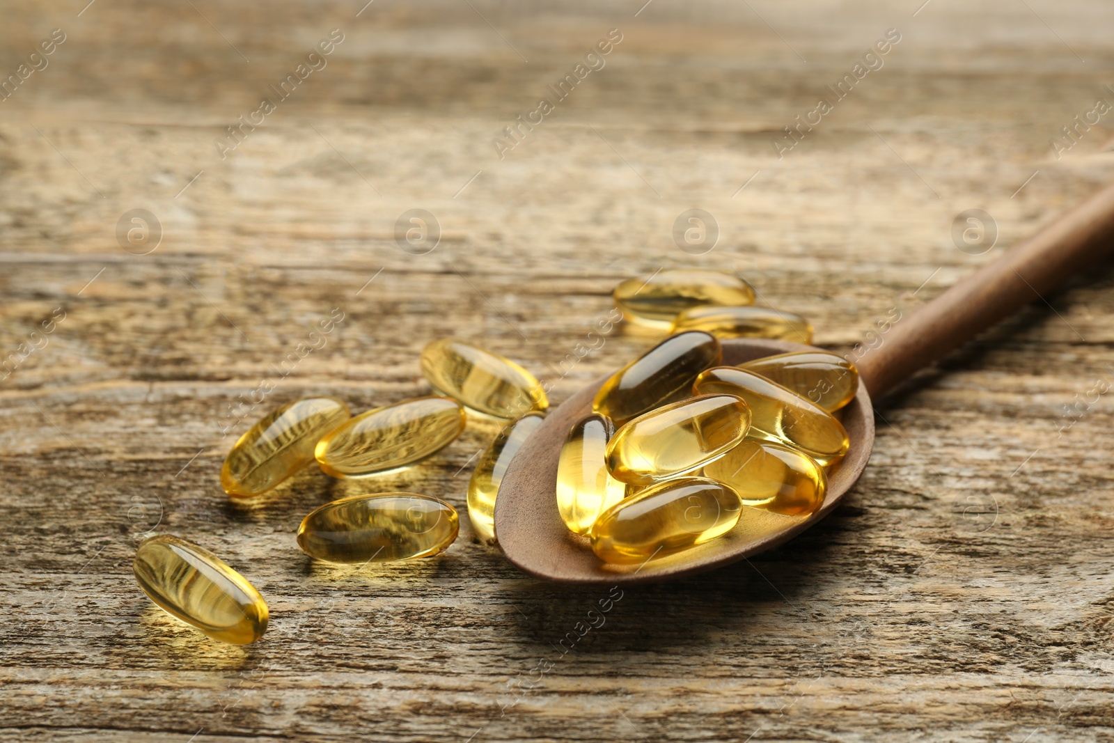 Photo of Vitamin capsules in spoon on wooden table, closeup