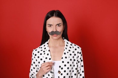Emotional woman with fake mustache on red background