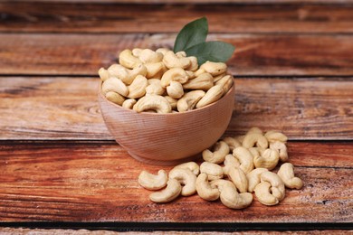 Photo of Tasty cashew nuts and green leaves on wooden table